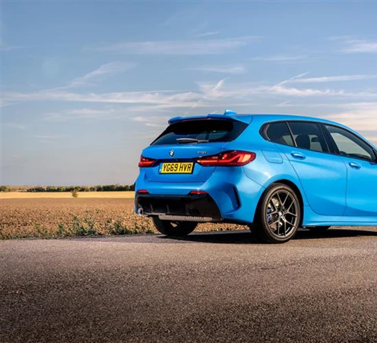 A blue BMW 1 Series car on a road with a field in the background on a sunny day